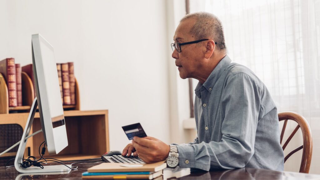 man holding his credit card looking at his computer